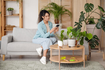 Beautiful young African-American woman taking pictures of her plants in living room