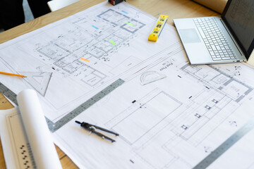 Architectural blueprints and drafting tools are on wooden table