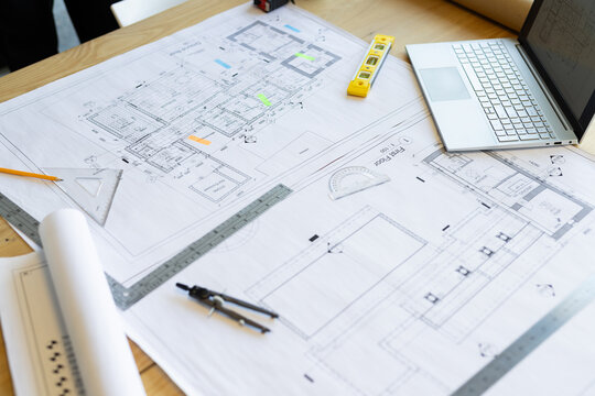 Architectural blueprints and drafting tools are on wooden table