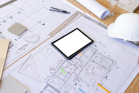 Architectural plans and drawings spread out on table with a tablet in center