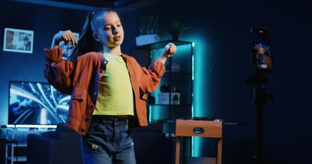 Panning shot of young charismatic kid taking part in trends filming content of her performing viral choreography on popular hit song using smartphone on tripod stabilizer