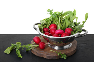 Metal colander with fresh radishes on black textured table against white background