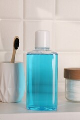 Bottle of mouthwash, toothbrush and cotton pads on white shelf in bathroom