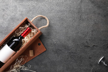 Bottle of wine in wooden box and corkscrew on dark textured table, flat lay. Space for text