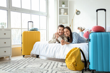 Young couple of tourists with bags lying on bed in hotel room