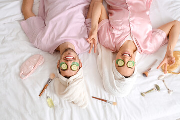 Young loving couple with cucumber slices and accessories lying on bed, top view