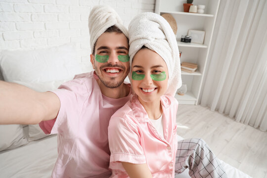 Young loving couple with under-eye patches taking selfie in bedroom, closeup
