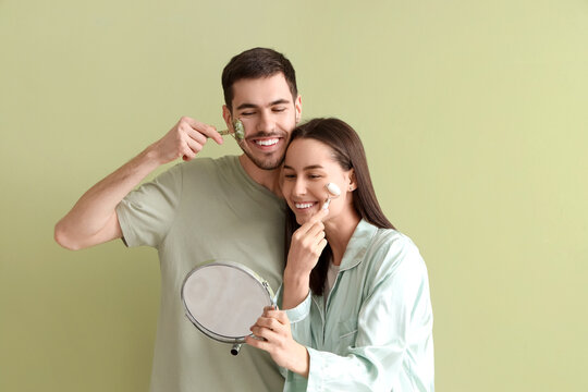 Young loving couple with facial massage tools and mirror on green background