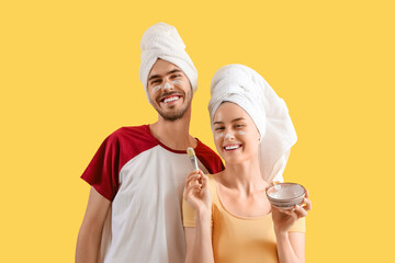Young loving couple with applied facial mask on yellow background