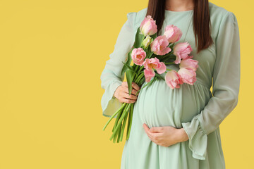 Young pregnant woman with tulips on yellow background, closeup