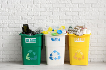 Full trash bins with different types of garbage near white brick wall. Recycling concept