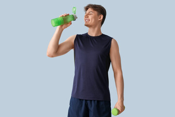 Sporty young man with bottle of water and dumbbell on light background