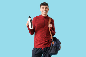Sporty young man with bottle of water and bag on blue background