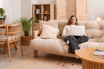 Young woman using laptop on soft sofa at home