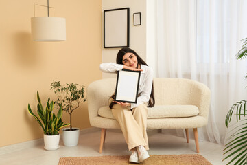 Young woman holding blank picture frame and sitting on sofa in living room