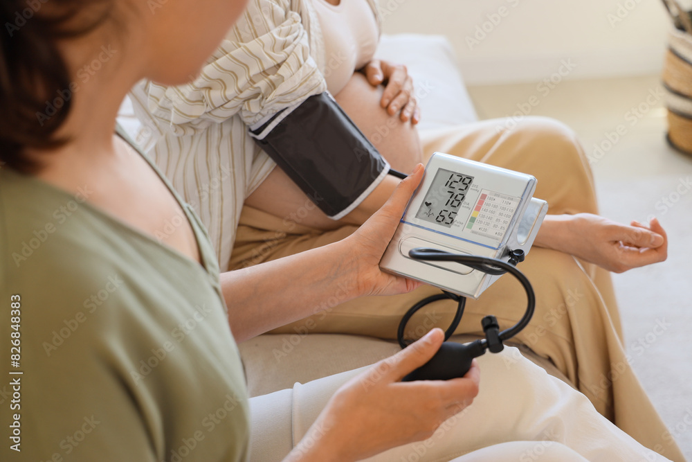 Canvas Prints young pregnant woman with doula measuring blood pressure on sofa at home, closeup