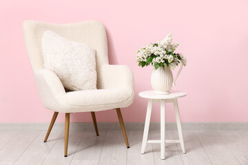 Armchair and vase with blossoming branches on coffee table near pink wall in living room