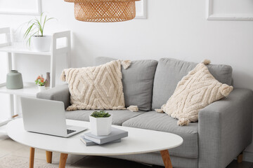 Stylish interior of living room with sofa and modern laptop on table