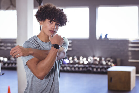 At gym, young biracial man stretching his arm while wearing smartwatch, copy space