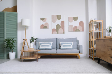 Interior of living room with comfortable sofa, coffee table and pictures on white wall