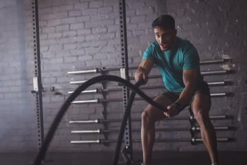 A strong and fit biracial man at gym training with battle ropes