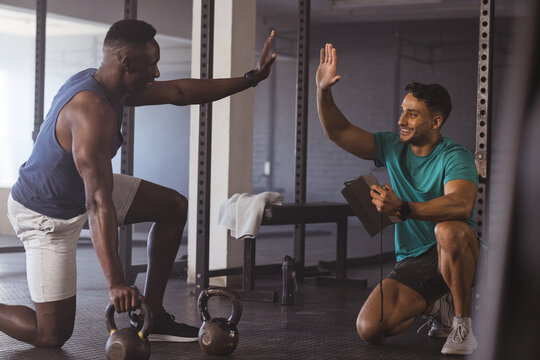 At gym, diverse men training with kettlebells, receiving guidance from fit trainer