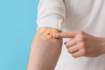 Male blood donor with applied patches on blue background, closeup