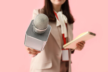 Female reporter with microphone and notebook on pink background, closeup