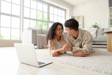 Young couple in love with laptop lying on floor at home