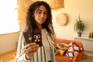 Young African-American witch with tarot cards and stones at home