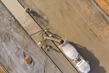 Concrete is poured from mixer truck for construction of pedestrian walkway by masonry workers