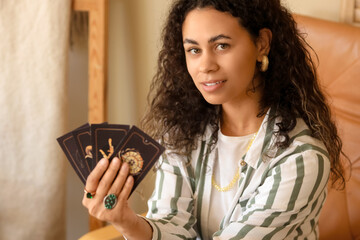 Young African-American witch with tarot cards at home, closeup