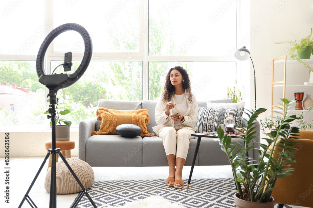 Wall mural young african-american witch with tibetan singing bowl recording video at home