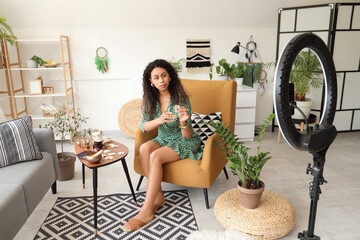 Young African-American witch with rune in armchair recording video at home