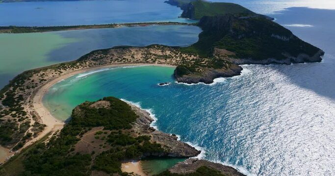 Capture of the stunning curved sandy shoreline and clear blue waters of Voidokilia Beach in Greece, surrounded by lush greenery and rocky formations.