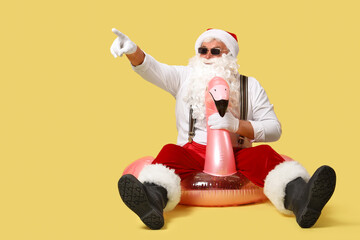 Santa Claus on swim ring pointing at something against yellow background. Christmas in July