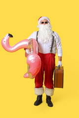 Santa Claus with swim ring and suitcase on yellow background. Christmas in July