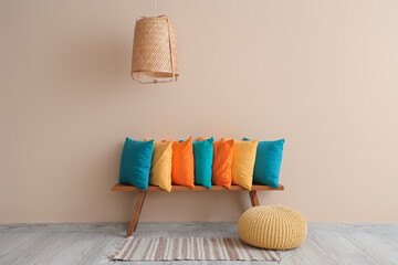 Colorful pillows on wooden bench and pouf near beige wall in room