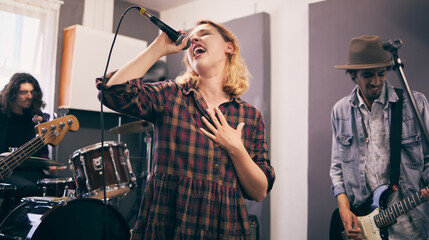 People, band and music practice with singer, microphone and electric guitar for concert rehearsal at home. Musician group, vocal training and recording song, track and audio with team work in garage