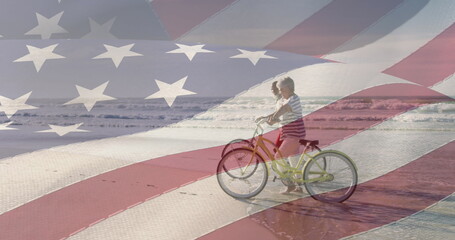 A young Caucasian boy is riding bicycle on a beach, overlaid with American flag