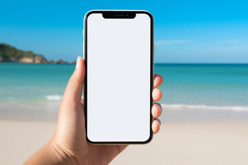 Hand holding a smartphone with a blank screen against a backdrop of a sunny beach and turquoise ocean, ready for mockup with copy space for customization or advertisement