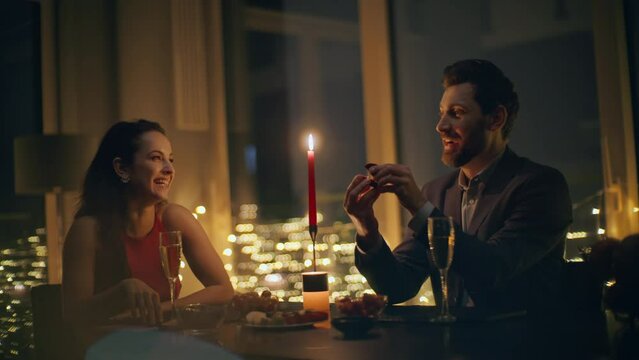 Happy guy proposing engagement wedding ring at big windows night hotel closeup