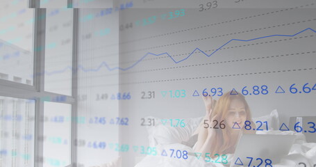 Fototapeta premium Image of trading board over beautiful caucasian woman lying on bed and talking on image call