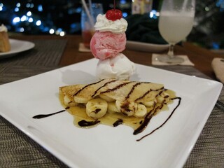 strawberry and vanilla ice cream wit whipped cream and cherry on top of banana crepe with chocolate sauce