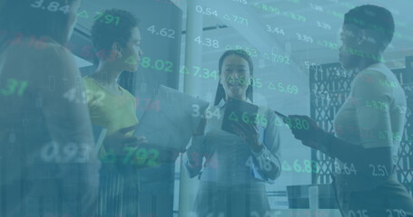 Image of trading board, diverse female coworkers discussing holding laptop and digital tablet