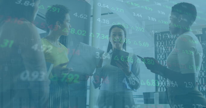 Image of trading board, diverse female coworkers discussing holding laptop and digital tablet