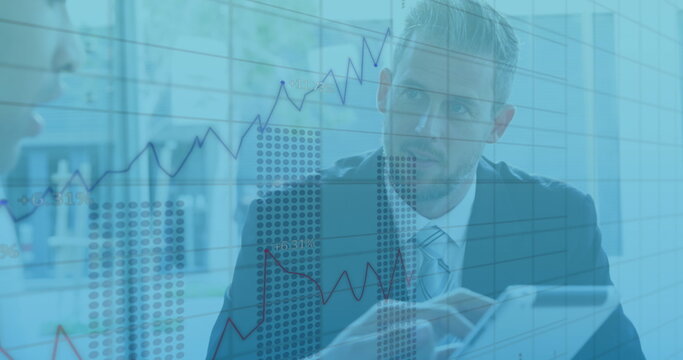 Image of graphs with changing numbers, diverse coworkers discussing report on digital tablet