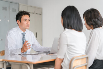 三者面談で厳しい話をする男性担任教師・先生と落ち込む生徒と保護者
