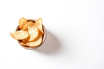 Close-up of a bowl filled with crispy potato chips. The chips are golden brown and look delicious. The bowl is on a white background, with a shadow cast to the right of the bowl.