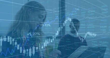 Image of multiple graphs moving over caucasian businesswoman using digital tablet in office